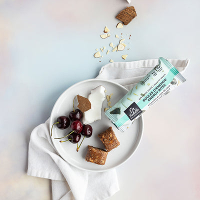 Photographie de deux boules énergie à l'amande et la noix de coco avec leur sachet. Des cerises et de la noix de coco fraîches apparaissent sur la photo. Photograph of two almond and coco energy bites and their bag. Cherry and coconut are also on the image. *conçu pour respecter les besoins des personnes atteintes de diabète, d'hypercholestérolémie ou d'hypertension artérielle